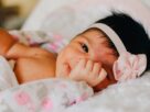 baby wearing white floral headband lying on bed while smiling