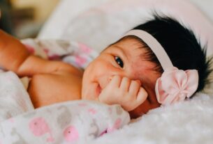 baby wearing white floral headband lying on bed while smiling